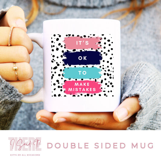 A person holding a white coffee mug with double sided print. The mug has a polka dot design on the side with the text 'It's ok to make mistakes'
