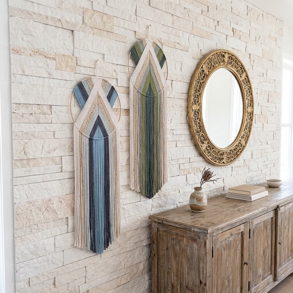 Two bohemian-style woven wall macrame wall hangings in blue, green, and beige tones are displayed on a light stone brick wall next to an ornate gold-framed mirror and a rustic wooden console table.