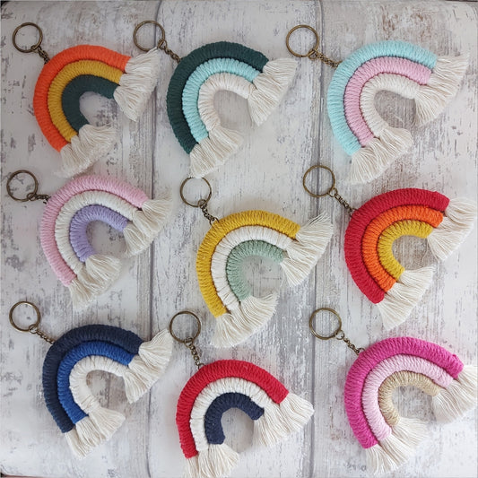 A collection of colourful macrame rainbow keyrings displayed on a white wooden surface.