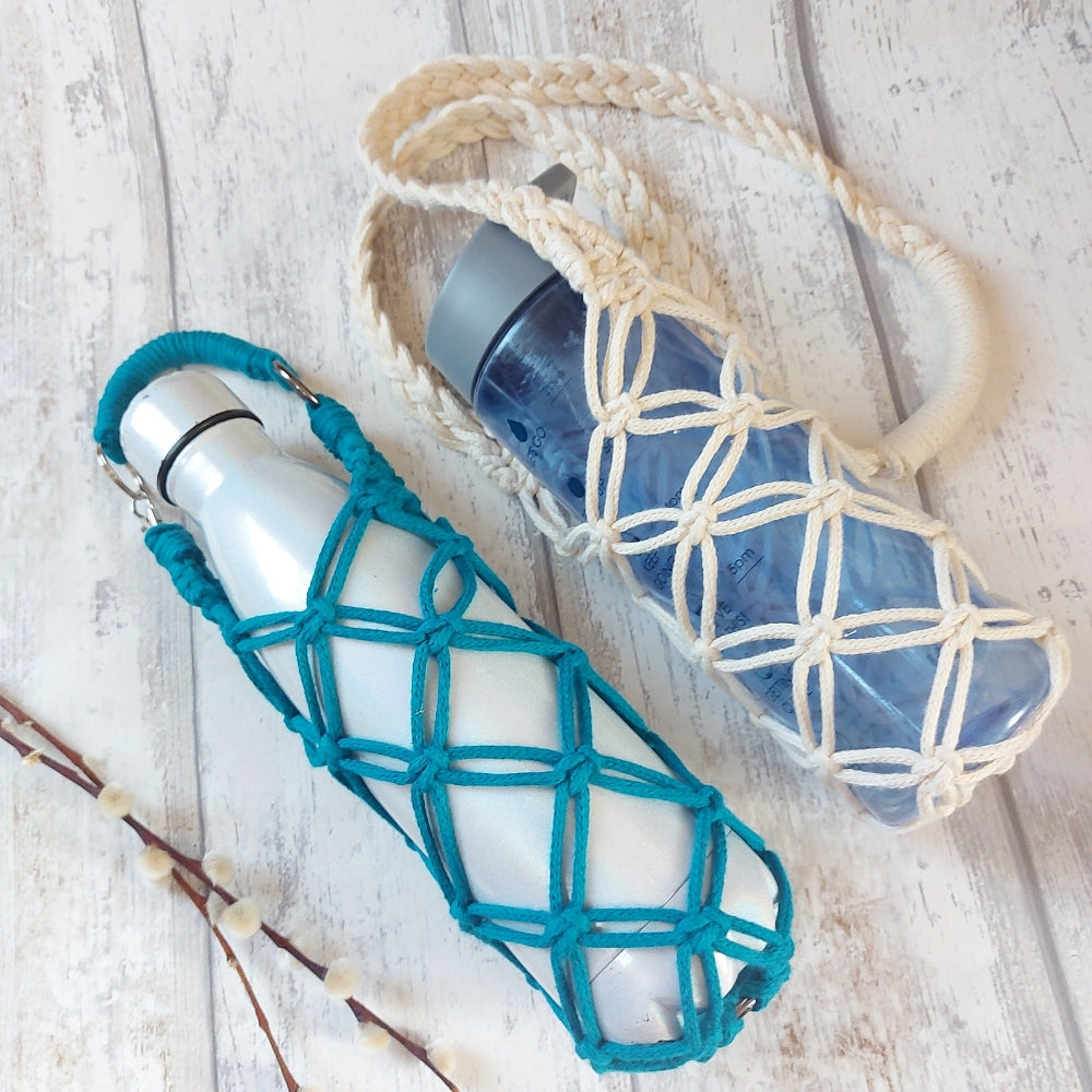 A blue macrame water bottle holder with a white cap, displayed next to a water bottle on a white wooden surface.