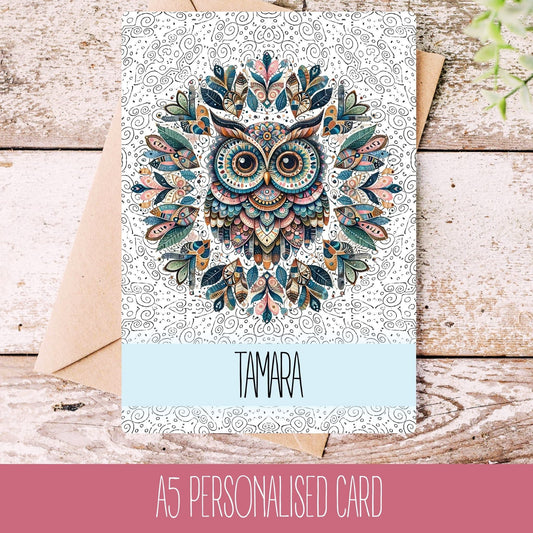 A personalised greeting card with a mandala owl design, featuring the name 'TAMARA' on the front, placed on a wooden background with a white envelope.