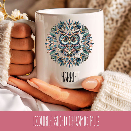 A ceramic coffee cup with a colourful mandala owl design and the name 'Harriet' printed on the side, held in a person's hand.