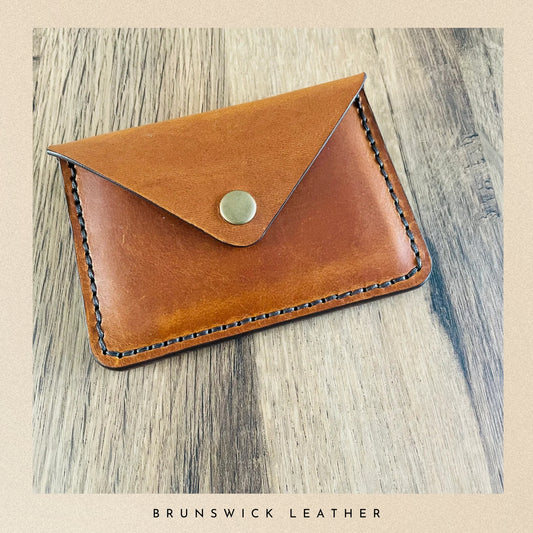 Brown leather cardholder on a wooden surface with 'Brunswick Leather' branding.