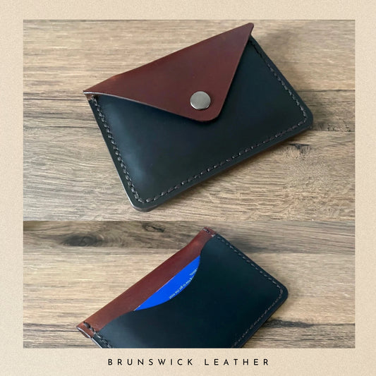 Black leather cardholder with brown flap on a wooden surface, branded 'Brunswick Leather'.