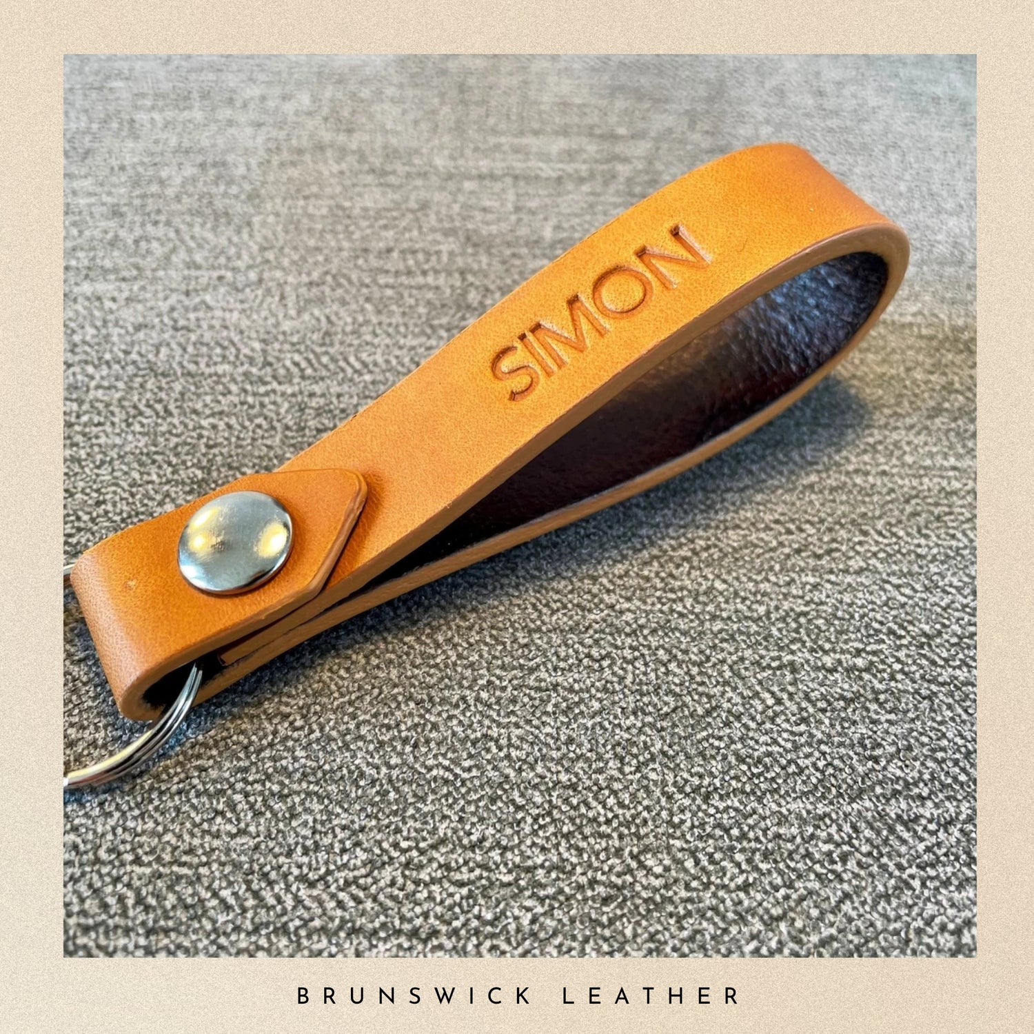 Brown leather key fob with 'SIMON' engraving on a textured surface, branded 'Brunswick Leather'.