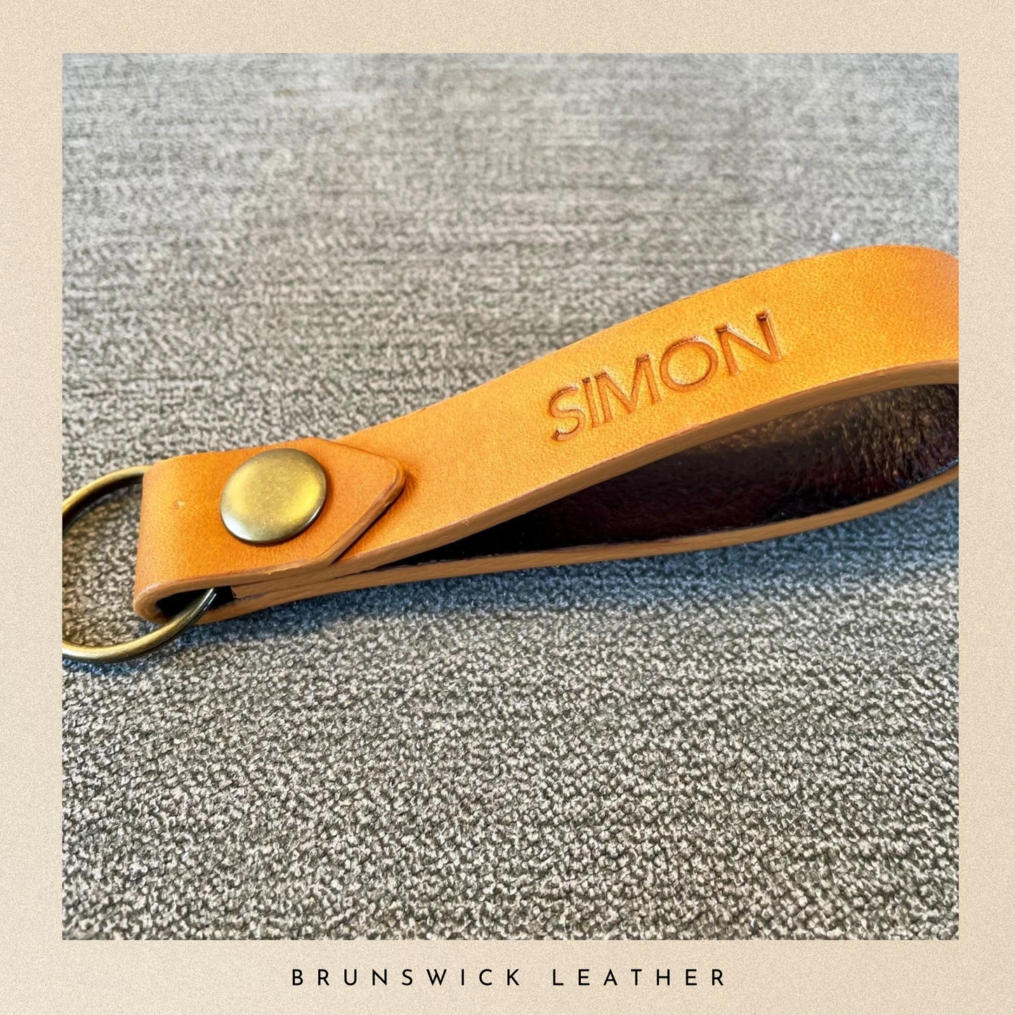 Leather keychain with 'SIMON' engraving on a textured surface, branded 'Brunswick Leather'.
