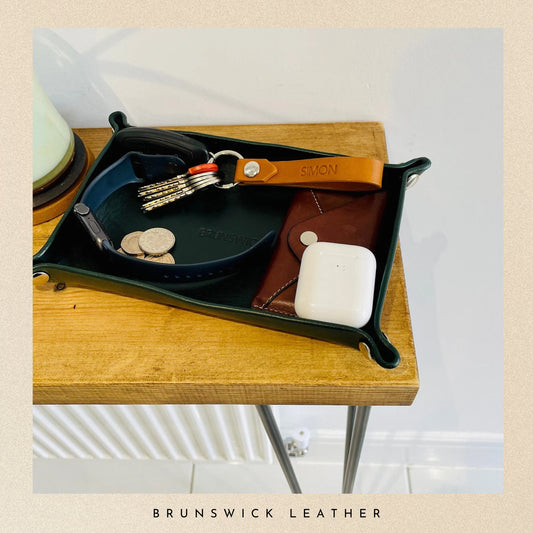 Tray with assorted items including a leather keychain on a wooden surface, branded 'Brunswick Leather'.