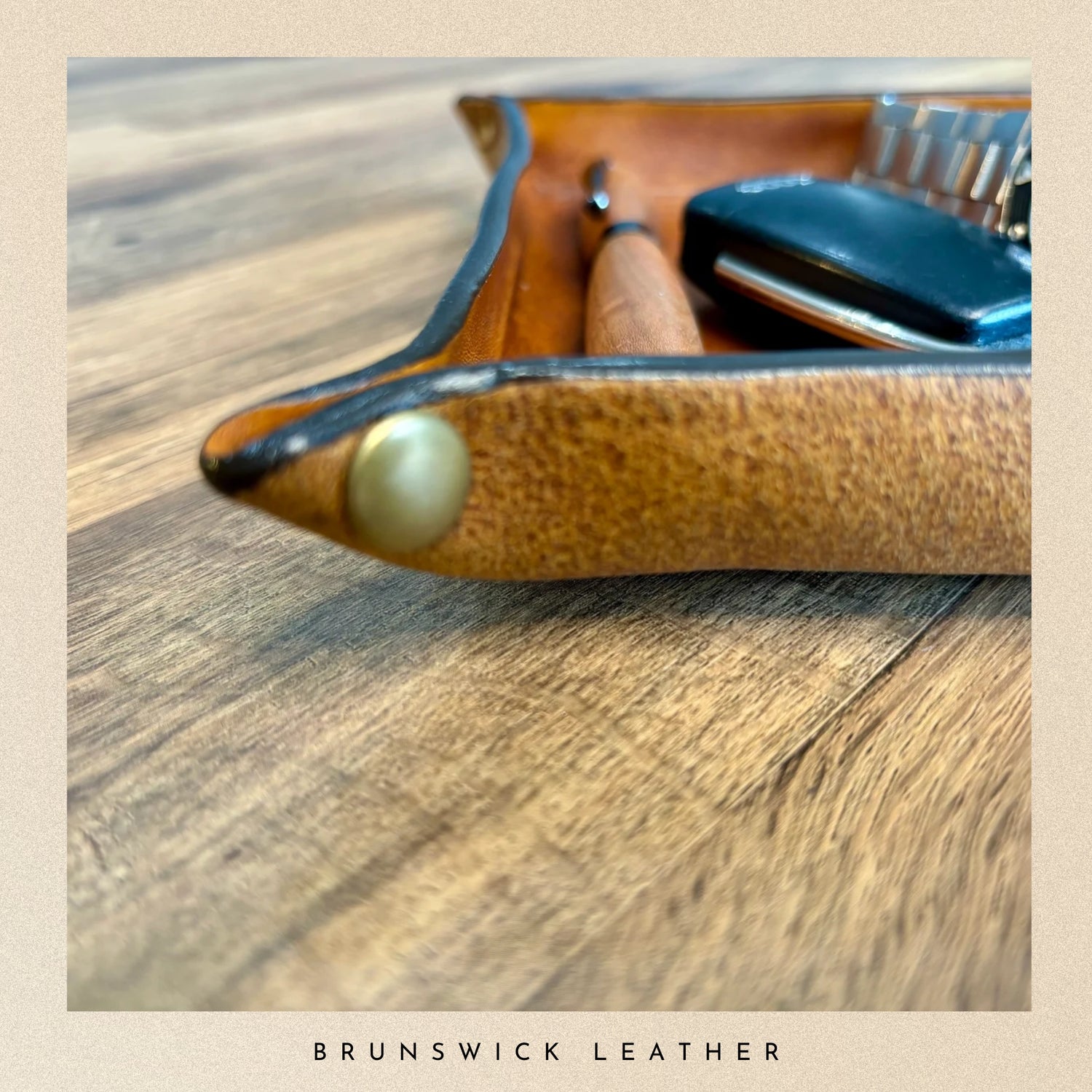 Brown leather case with a gold button on a wooden surface, featuring the brand 'Brunswick Leather'.