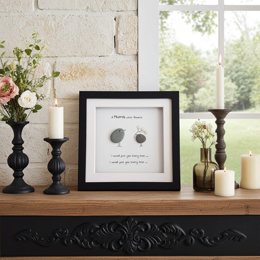 Decorative setup with framed pebble artwork, candles, and flowers on a mantelpiece.