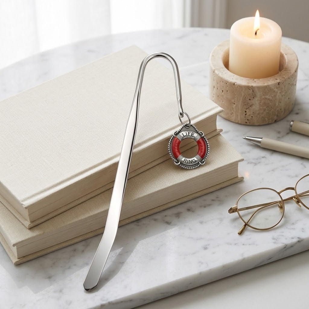 A silver metal bookmark with a red and white life preserver ring charm, resting on stacked beige books on a white marble surface.