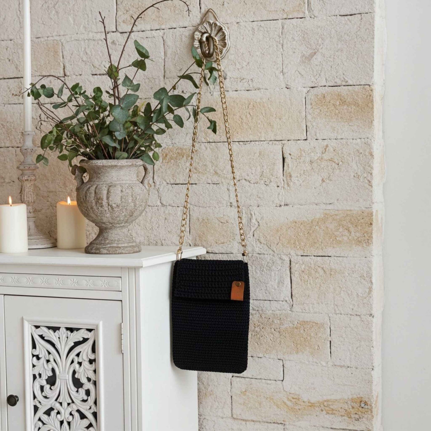 Navy woven handbag with a gold chain strap hanging on a stone wall next to a white cabinet.