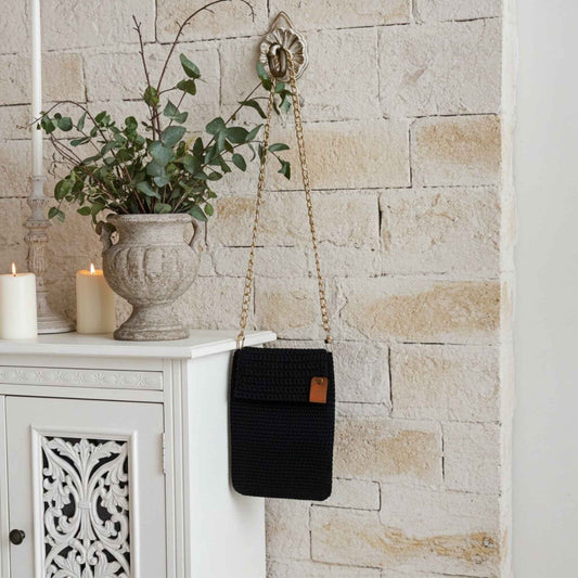 Navy woven handbag with a gold chain strap hanging on a stone wall next to a white cabinet.