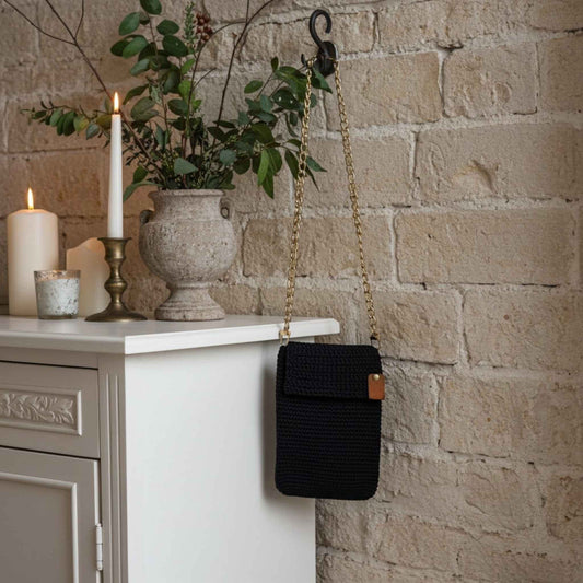 Navy handbag with a gold chain strap hanging on a hook against a stone wall with candles and a vase.