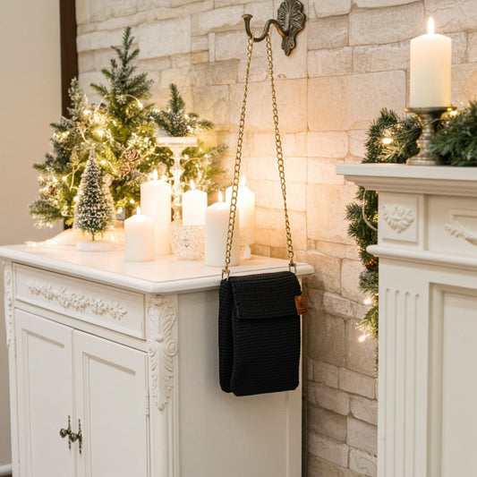 Decorative setting with candles, Christmas trees, and a navy phone handbag on a white cabinet against a stone wall.