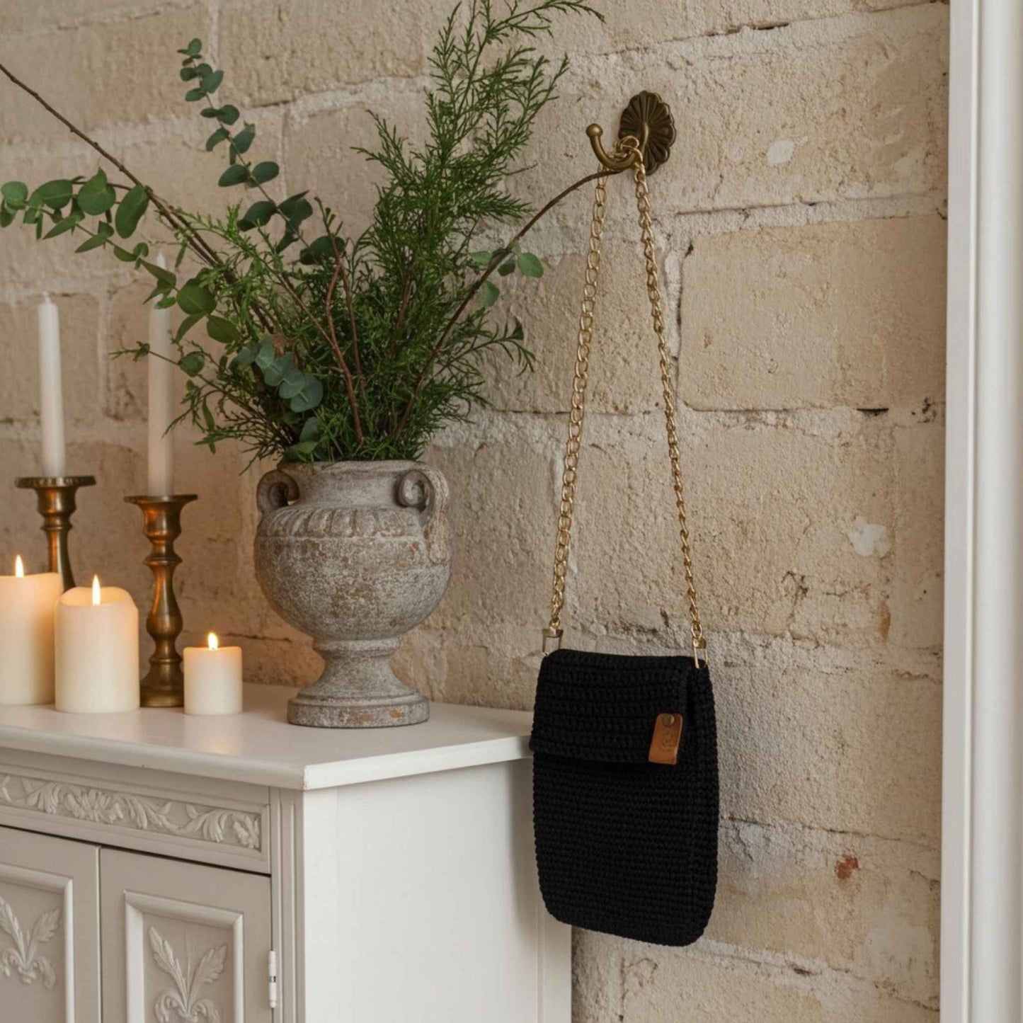 Navy woven bag hanging on a wall hook next to a stone wall with a decorative urn and candles.
