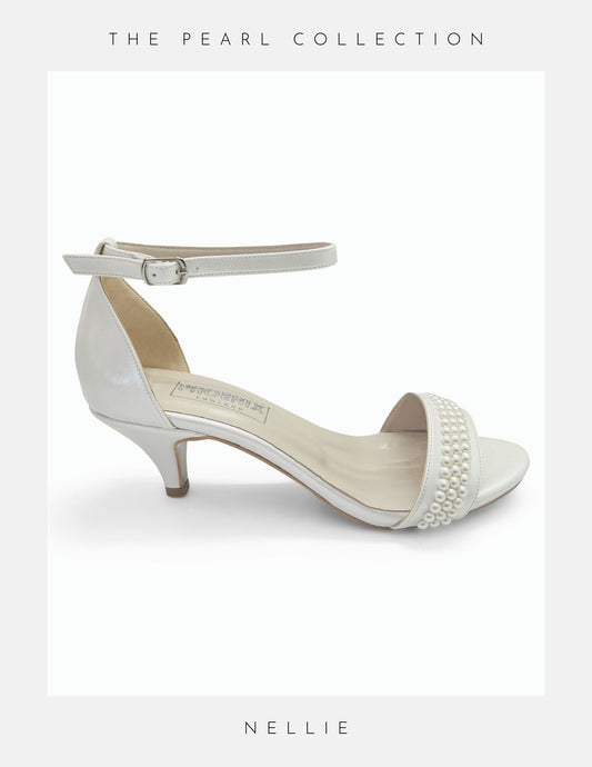 A white kitten heel bridal shoe with pearl embellishments and an ankle strap, from the 'Pearl Collection' labeled as 'Nellie'.