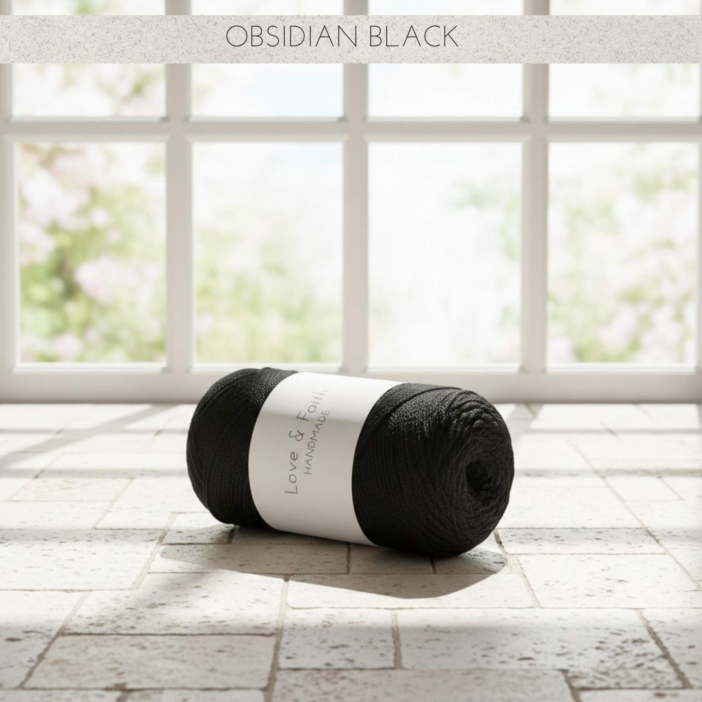 Ball of Obsidian Black yarn on a wooden floor with a window in the background