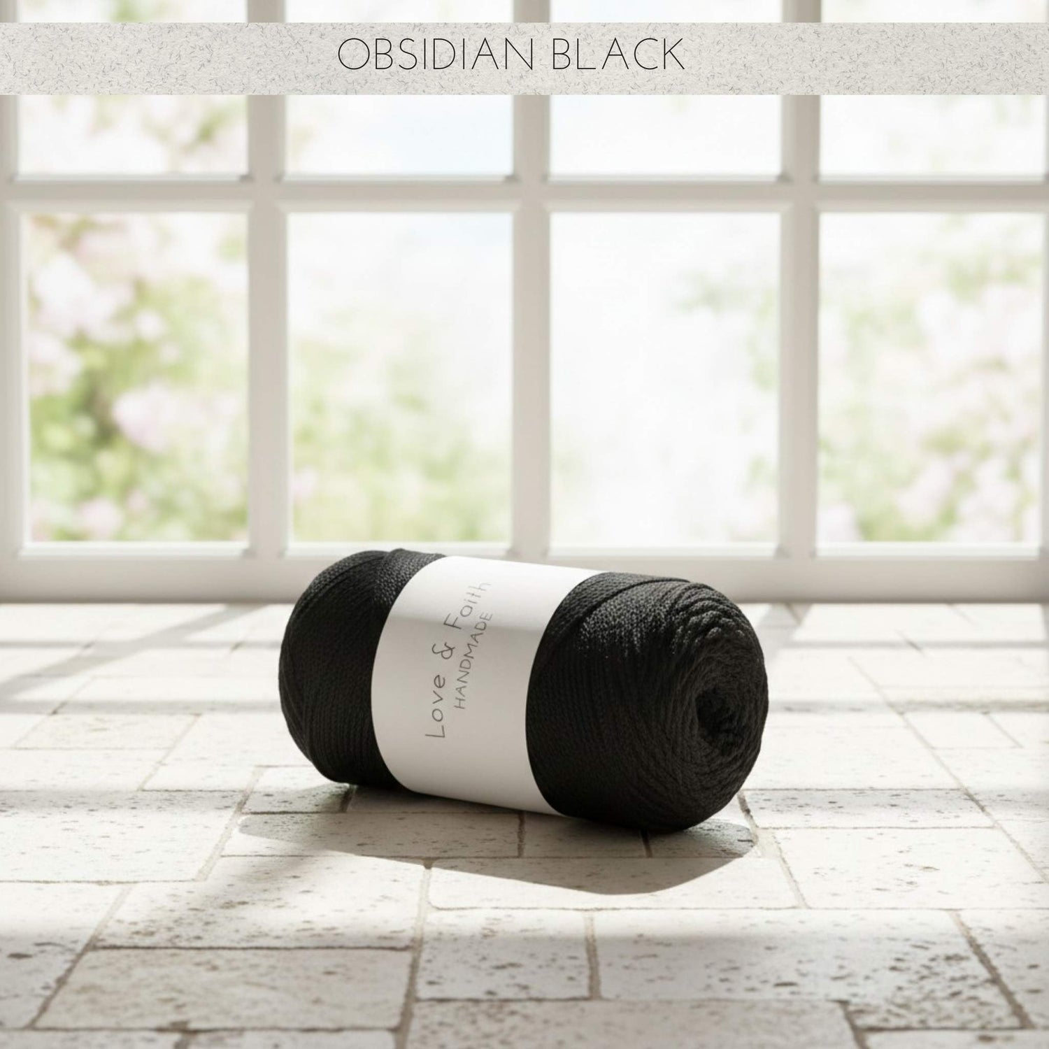 Ball of Obsidian Black yarn on a wooden floor with a window in the background