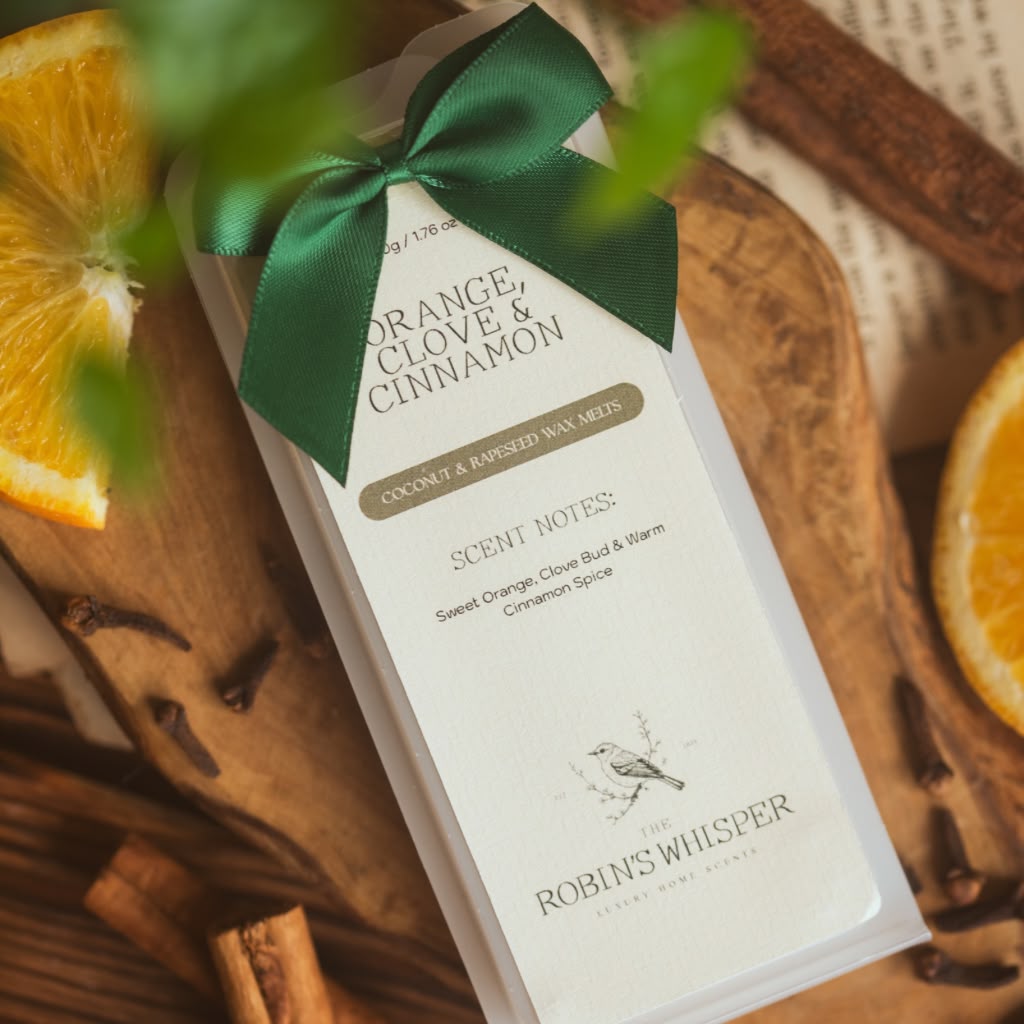 Product packaging of wax melts with a green ribbon on a wooden surface with oranges and cinnamon sticks.