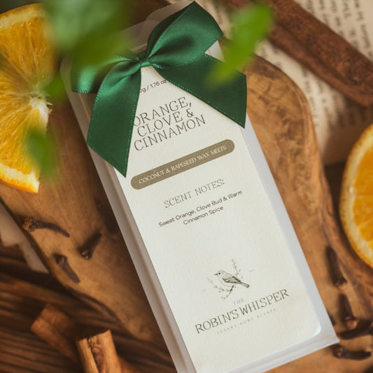 Product packaging of wax melts with a green ribbon on a wooden surface with oranges and cinnamon sticks.