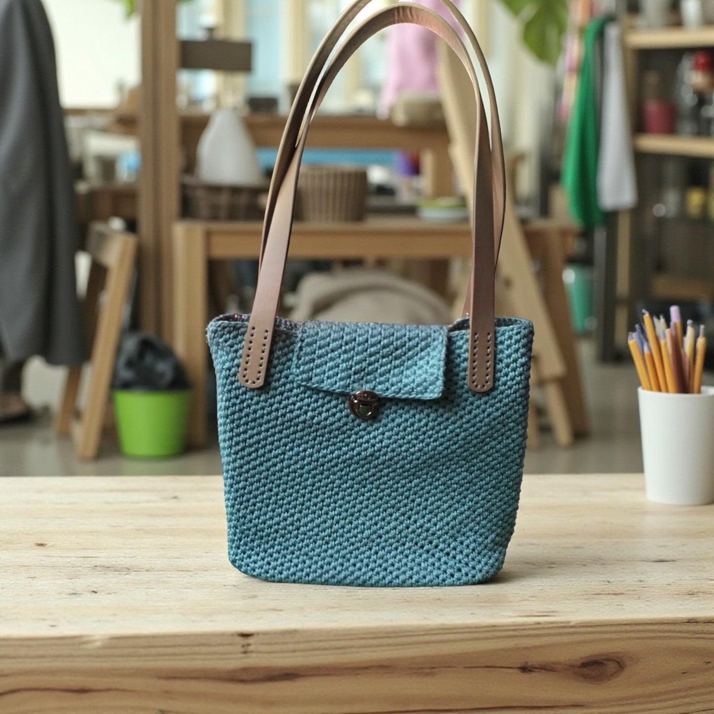 Blue crochet shoulder bag with brown handles on a wooden table in a shop setting