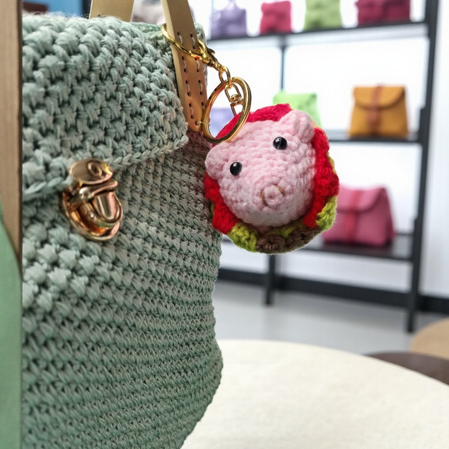 crochet shoulder bag with a pink pig keychain blurred background of shelves.