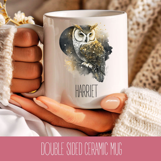 A white ceramic mug with a printed owl design and a name 'HARRIET' on it, held in a person's hand.