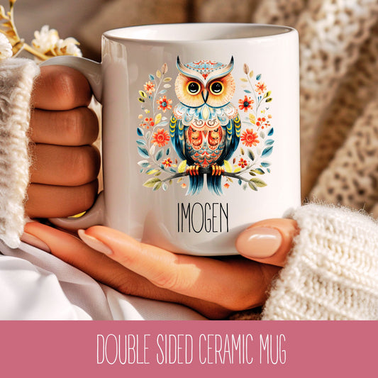 A double-sided ceramic mug with a colourful illustration of an owl surrounded by flowers and leaves, held in a hand. The name 'Imogen' is printed on the mug.