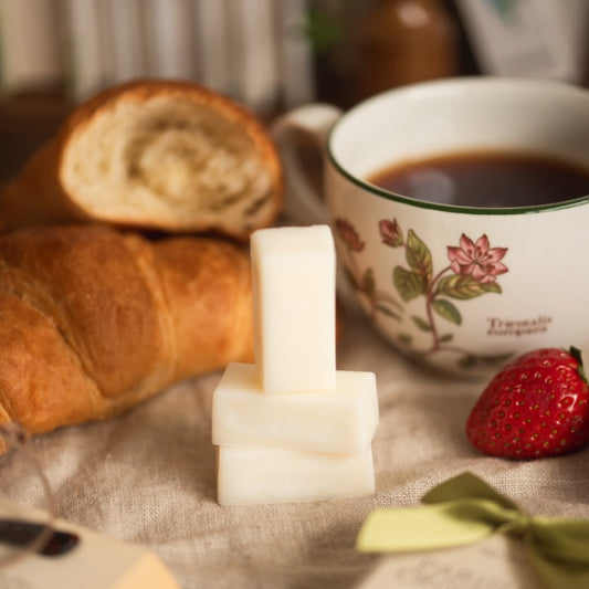 Tea cup with floral design, croissant, strawberry, and white wax melts on a textured surface.
