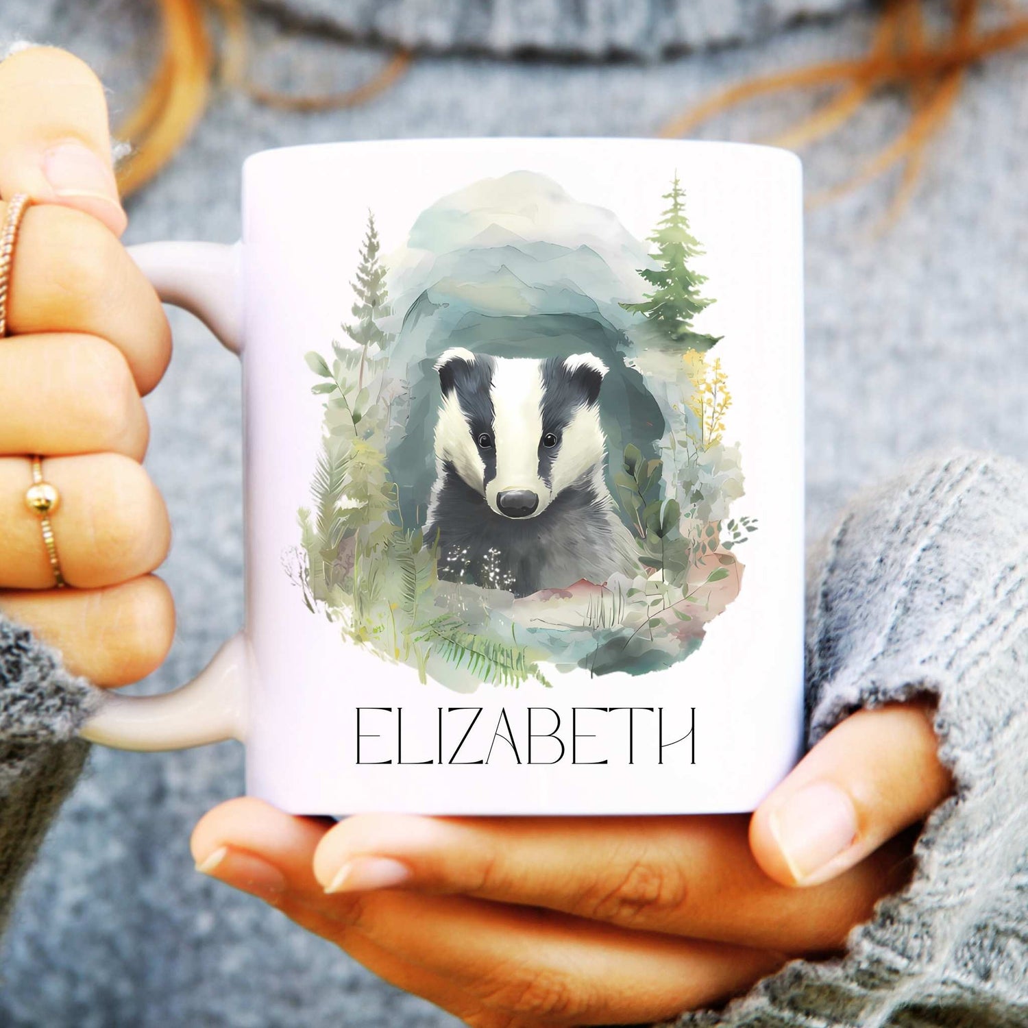 Person holding a mug with a badger illustration and the name 'ELIZABETH'.