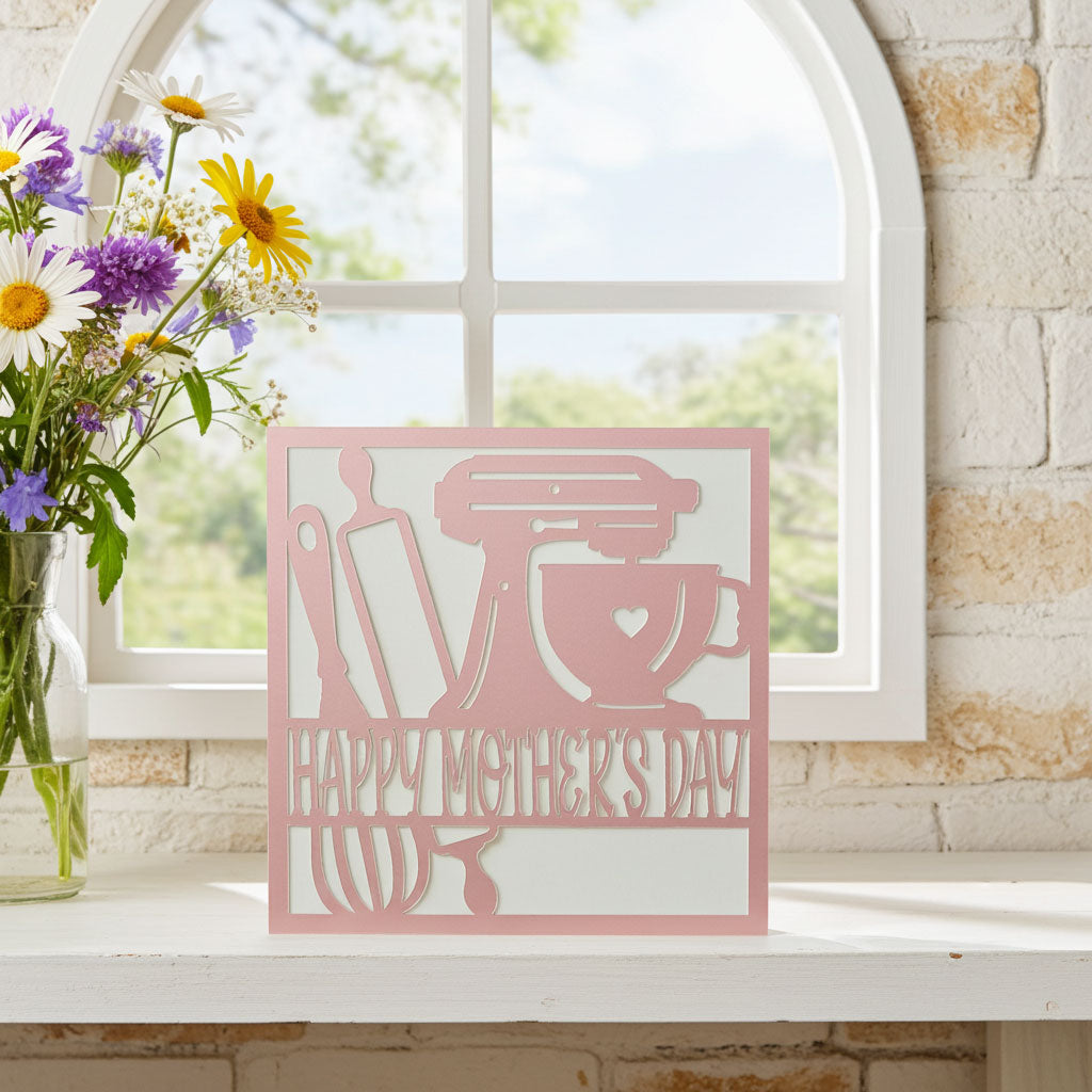 Pink baking card with kitchen-themed design in front of a window with flowers.