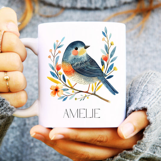 Person holding a mug with a bird illustration and 'AMELIE' text