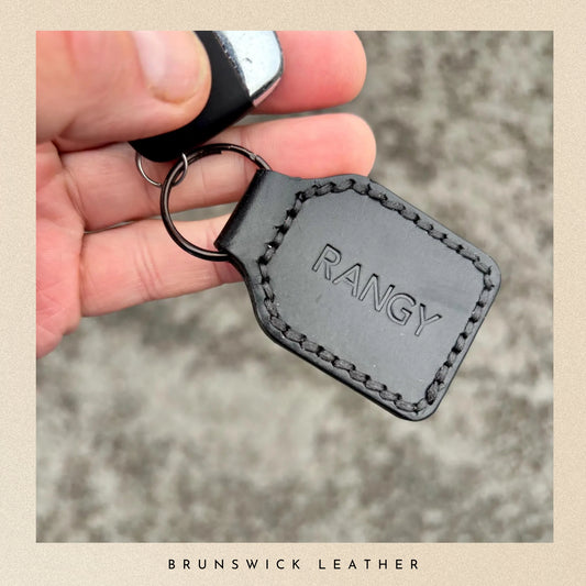 Black leather keychain with 'RANGY' branding held in a hand against a blurred background.