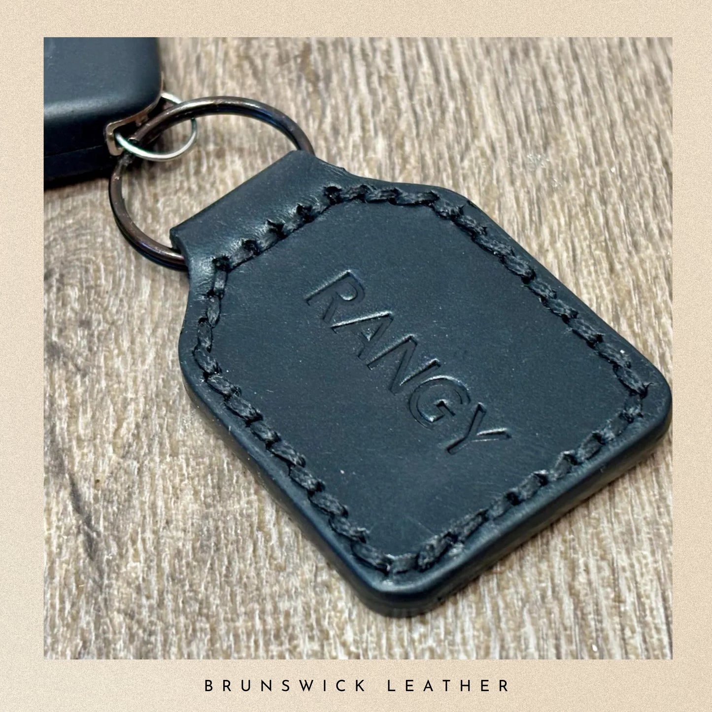 Black leather key fob with 'RANGY' embossed on it, placed on a wooden surface.