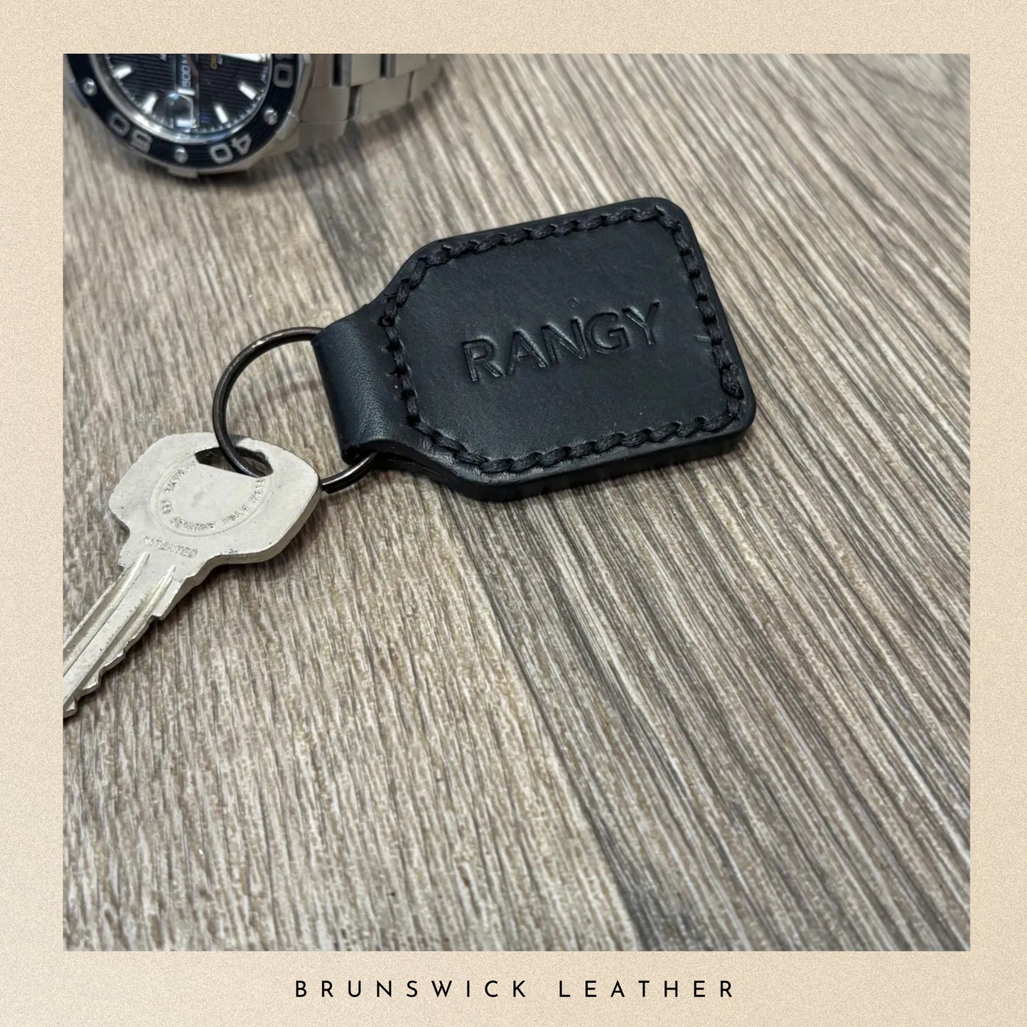 Black leather keychain with 'RANGY' branding on a wooden surface, featuring a key and watch.