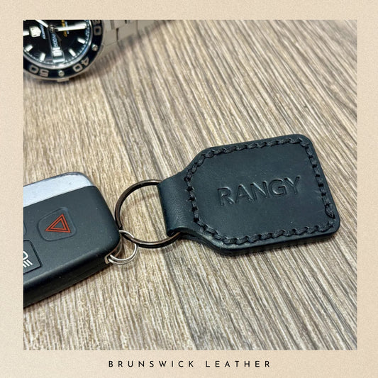 A personalised black key fob holding a car key on a wooden surface