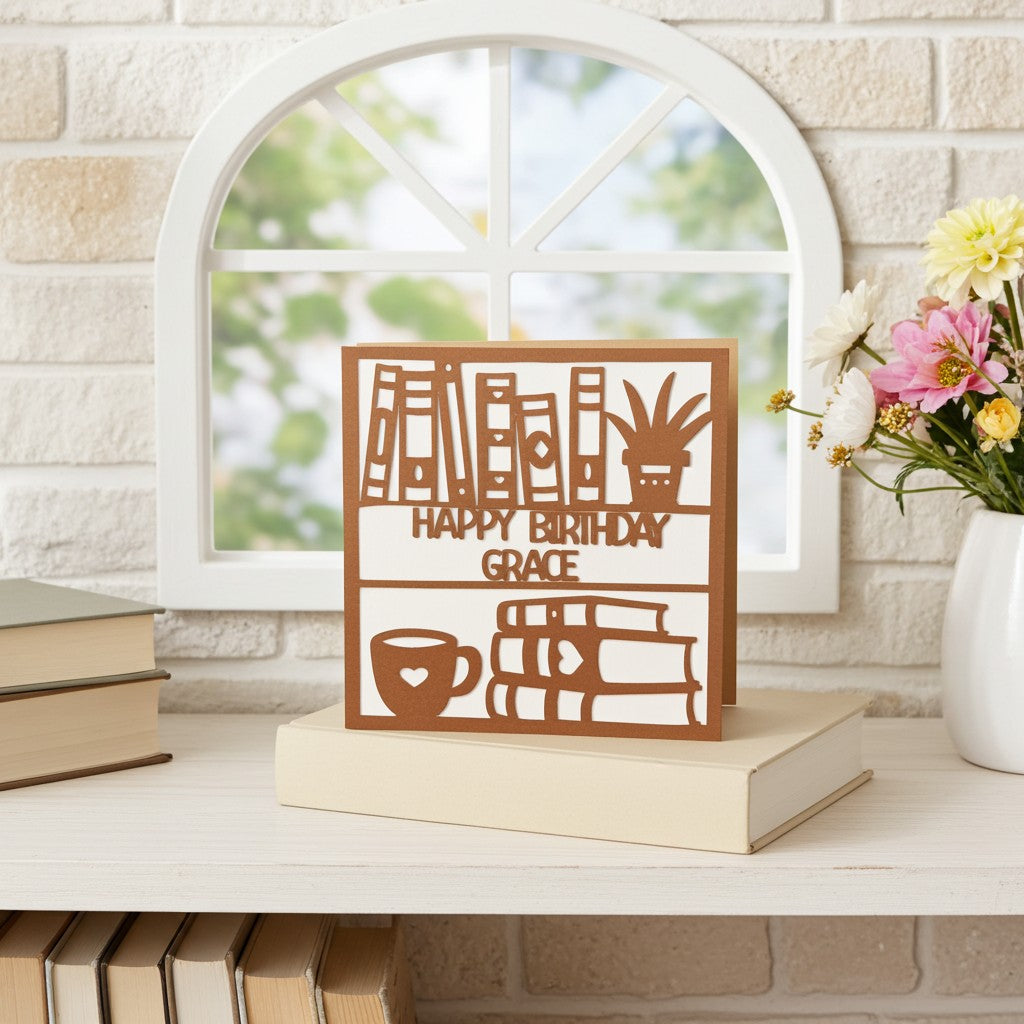 Personalised bookish birthday card with cut-out designs on a stack of books with a window and flowers in the background.
