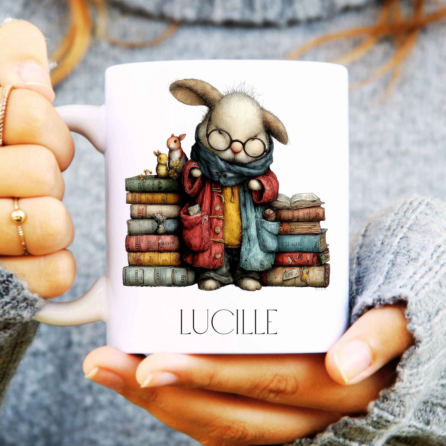 Mug with a rabbit character holding books, held by hands wearing textured sleeves.