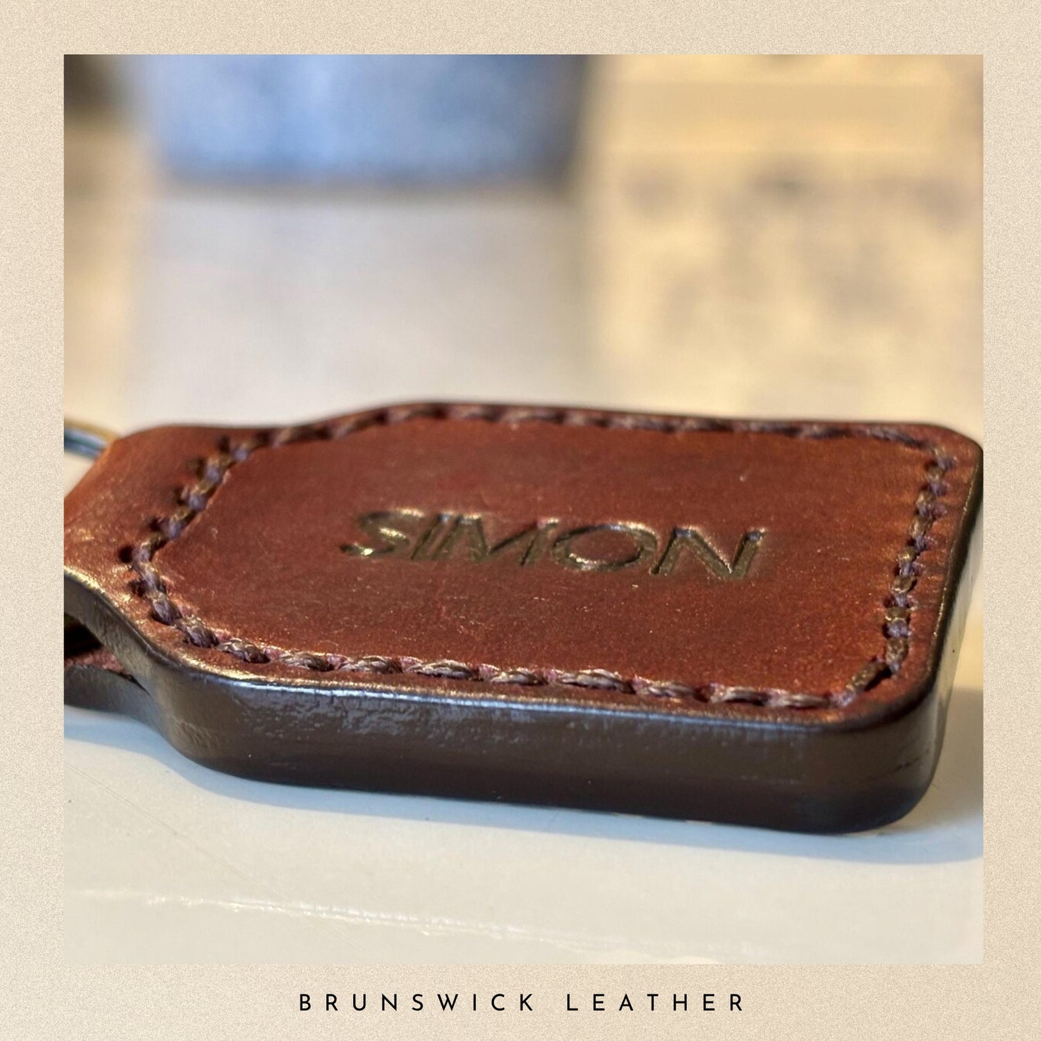 Brown leather keychain with 'SIMON' engraving on a blurred background