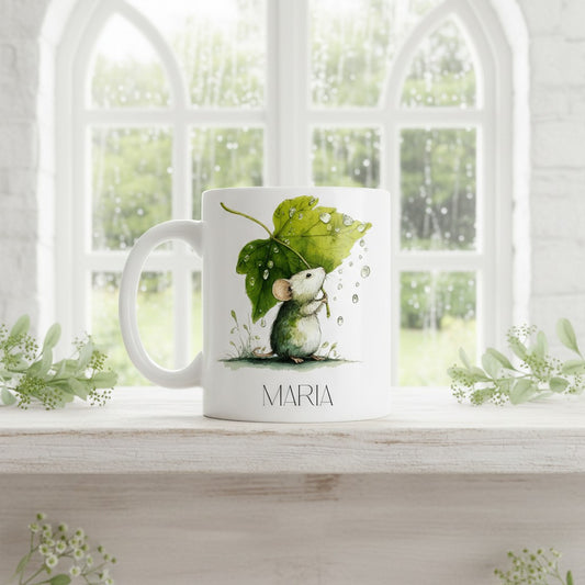 White mug with a mouse and leaf design on a windowsill with a view of greenery outside.