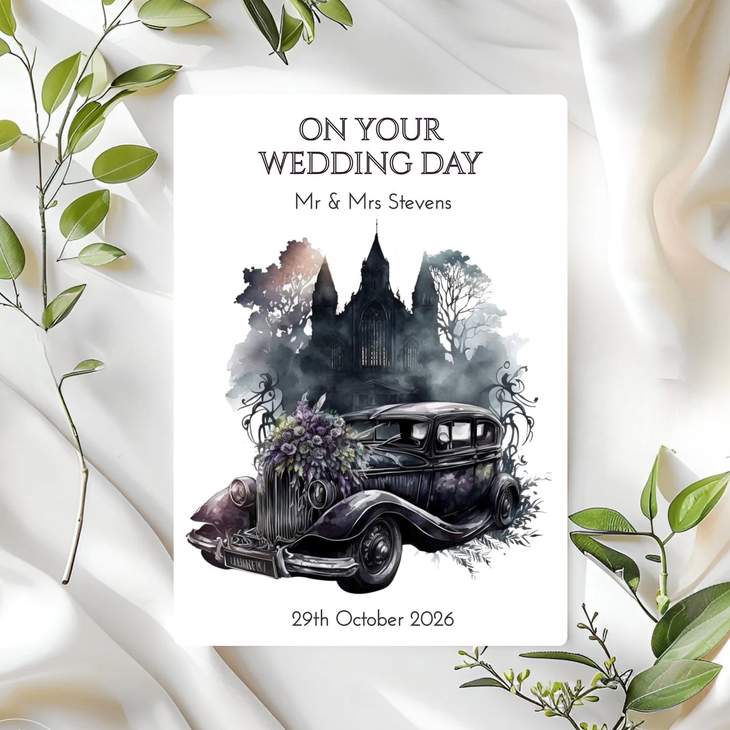 Wedding card with vintage car and castle illustration on a white fabric background with green leaves.