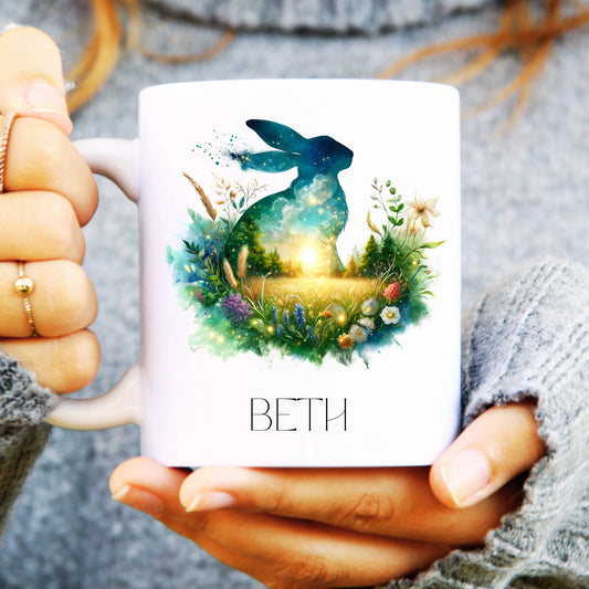 Person holding a mug with a hare and floral design, featuring the name 'BETH'.