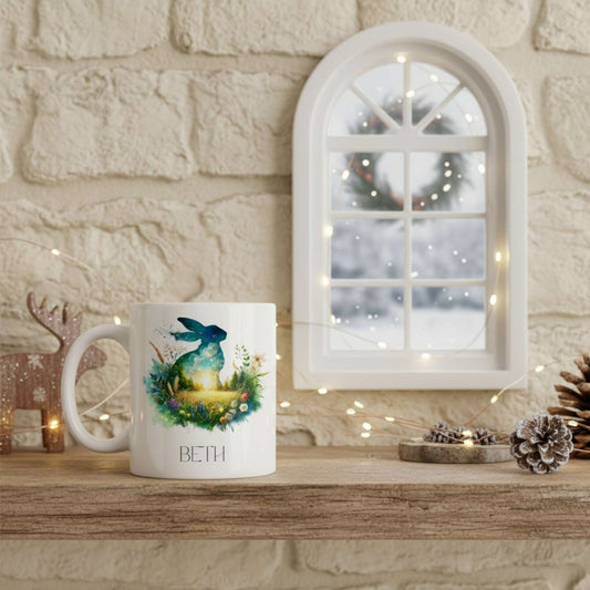 White mug with a hare design and 'BETH' text on a wooden surface with decorative festive items.