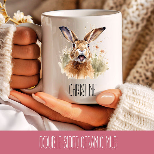 A ceramic mug with a double-sided design featuring a watercolor illustration of a hare on the front, personalized with the name 'Christine'.