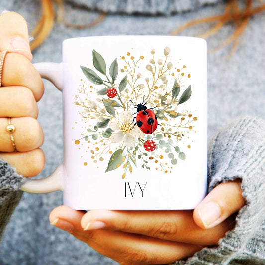 White mug with a ladybird and floral design held by a person wearing a gray sweater.