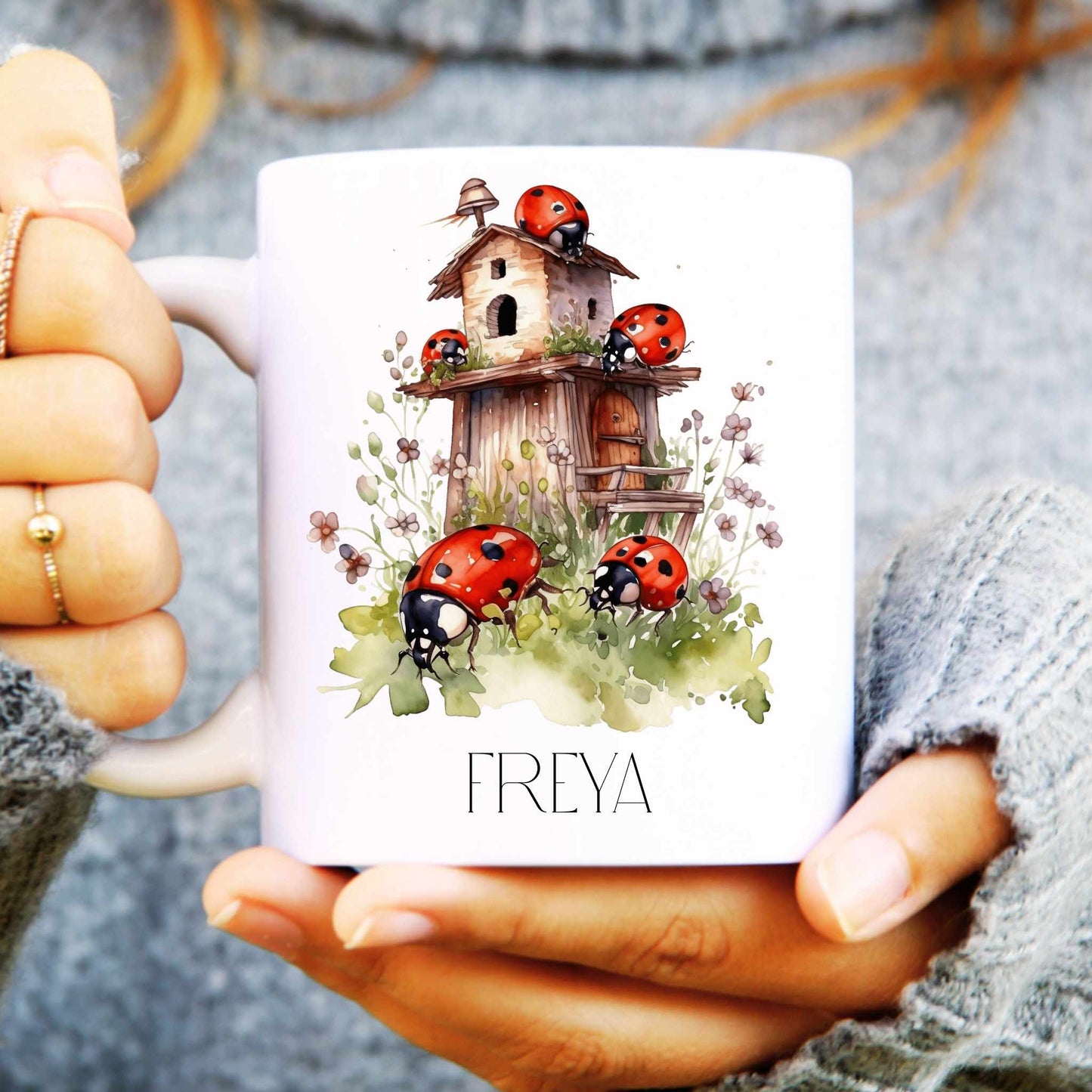 White mug with a design of ladybirds and a birdhouse, held by a person.