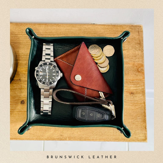 Green leather tray with a watch, wallet, coins, and car keys on a wooden surface, branded 'Brunswick Leather'.