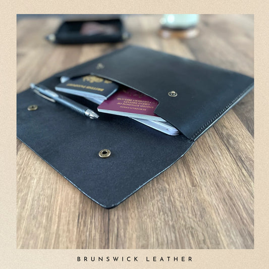 Black leather wallet with cards and a pen on a wooden surface, branded 'Brunswick Leather'.
