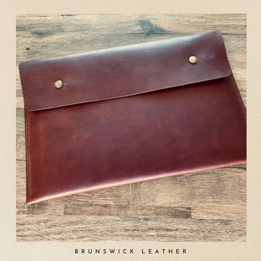 Brown leather clutch on a wooden surface with 'Brunswick Leather' branding.
