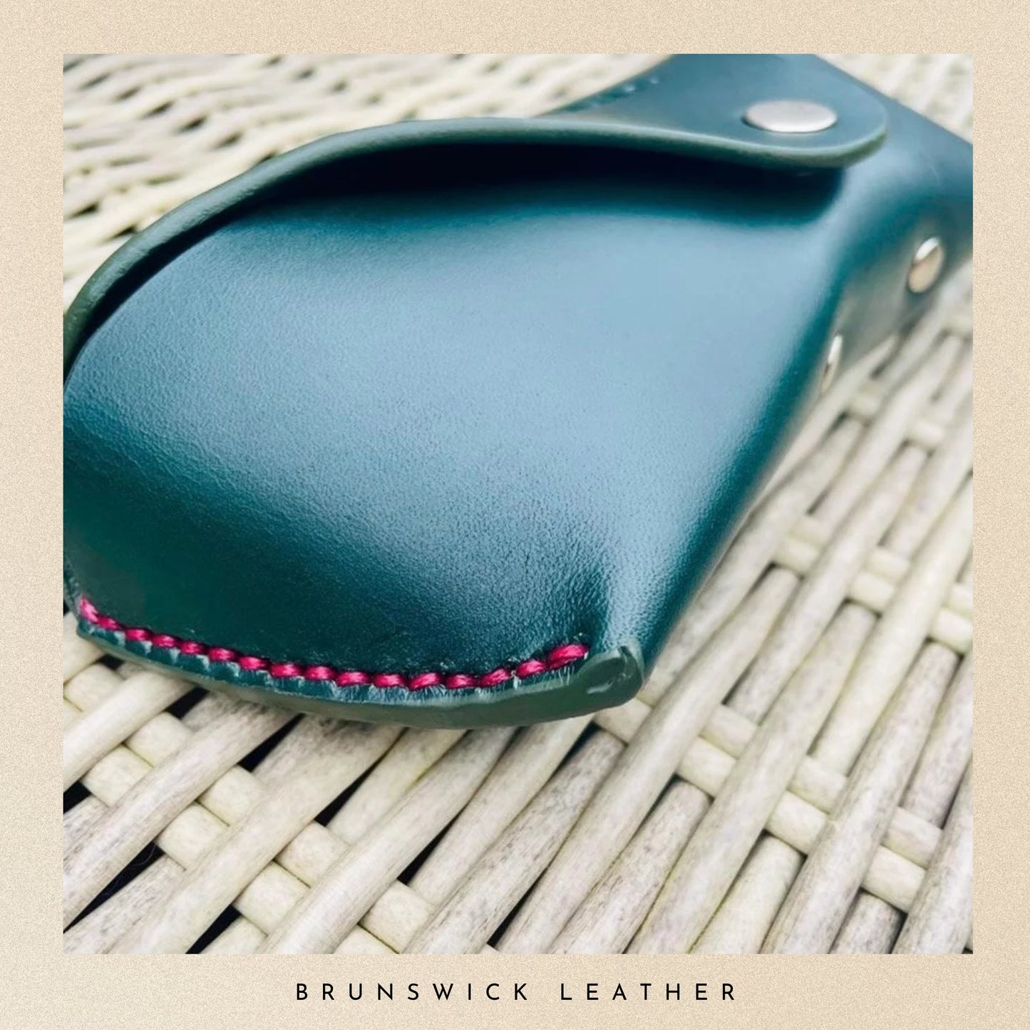 Teal leather case with pink stitching on a woven surface, branded 'Brunswick Leather'.
